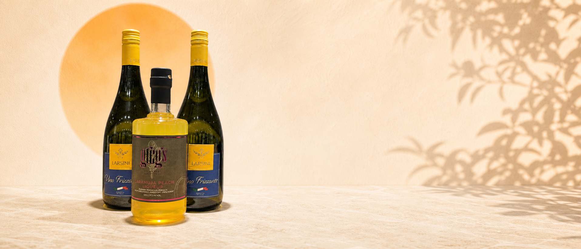 Greg’s Caramuja Peach Aperitif mit zwei Flaschen Larsini Vino Frizzante in heller sommerlicher Kulisse.